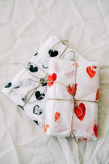 two gifts wrapped in homemade wrapping paper with red and black hearts tied with jute thread for Valentine's day on a white table