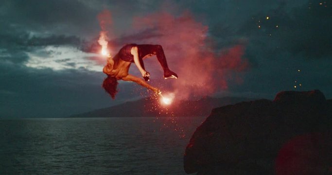 Extreme cliff jumping man backflipping off of an sea cliff with burning red hot flares at night, epic stuntman moments, people are awesome
