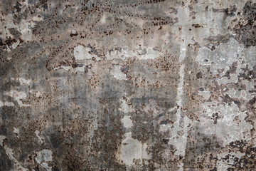 Rough textured cement concrete  wall with varying shades of gray, brown and cream with peeling layers