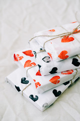 a stack of gifts wrapped in homemade wrapping paper with red and black hearts tied with jute thread for Valentine's day on a white table