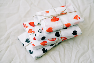 a stack of gifts wrapped in homemade wrapping paper with red and black hearts tied with jute thread for Valentine's day on a white table