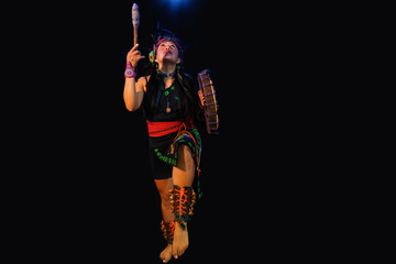 young woman Teotihuacana, Xicalanca - Toltec in black background, with traditional dress dance with a trappings with feathers and drum