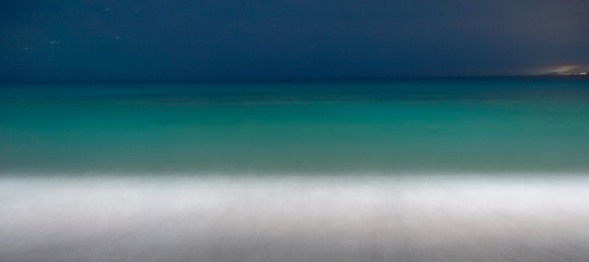 Summertime pebbly beach at the twilight. Soft evening light reflecting on blue sea water and small waves with foam. Seascape. Panoramic banner.