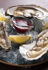 Seafood. Oysters with lemon and raspberry sauce in a plate with ice on a dark brown background. Background image, copy space © Nadia