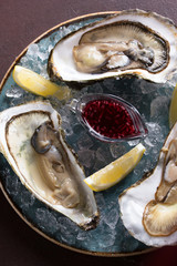 Seafood. Oysters with lemon and raspberry sauce in a plate with ice on a dark brown background. Background image, copy space © Nadia