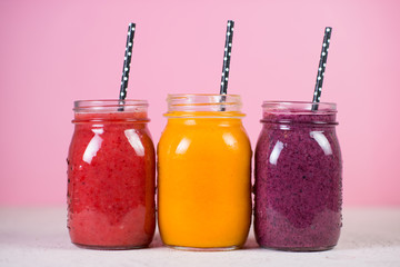 Set of colored fresh fruit smoothies on a light pink background.