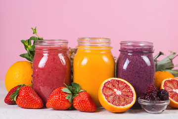 Fototapeta na wymiar Set of colored fresh fruit smoothies on a light pink background.