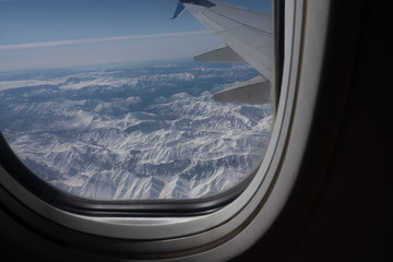 Snowed mountain tops aerial landscape view through aircraft illuminator