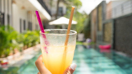 Woman holding orange juice near the pool on holidays in luxury hotel.Travel concept.