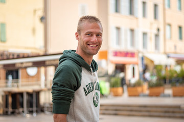 Portrait beau gosse charmant jeune homme caucasian blond aux yeux bleu joyeux et confiance en soi séduisant chanceux charismatique européen heureux zen à pull vert sourire aix en provence