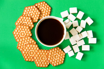 Cup of black coffee with cookies and refined sugar on a green background. View from above