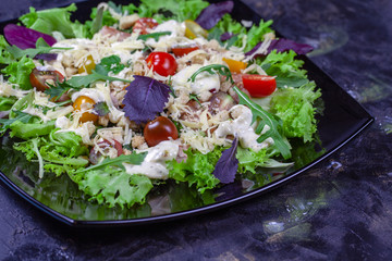 Caesar salad with croutons, quail eggs, cherry tomatoes and grilled chicken on a black background