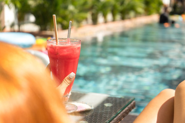 Summer vacation style red haired beautiful woman holding watermelon juice near the pool on holidays .Travel concept.