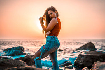 Lifestyle, a young woman in a red shirt and torn jeans on a sunset on the coast with the sun in the background