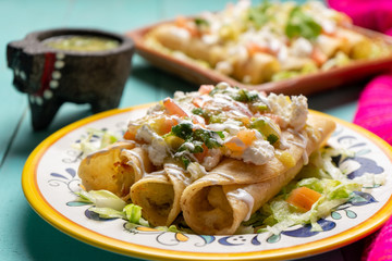Mexican potato and cheese fried tacos also called flautas with green sauce on turquoise background