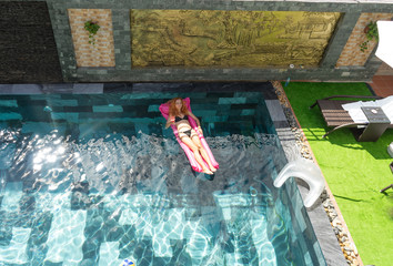 Top view of the red haired slim girl in bikini swimming on the pool and laying on the mattress in the hotel.Women is relaxing on the swimming pool in sunny day.