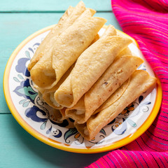 Mexican potato and cheese fried tacos also called flautas on turquoise background