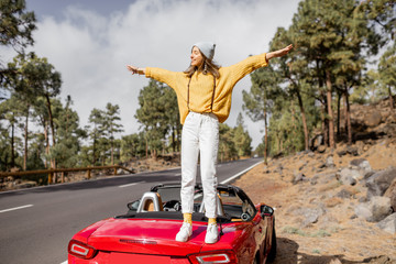 Portrait of a young stylish woman dressed in bright sweater traveling by car, enjoying beautiful...
