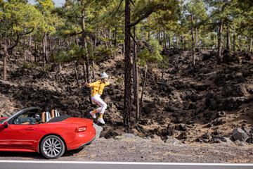Young stylish woman traveling by car, jumpimg from the car trunk on the roadside in the forest....