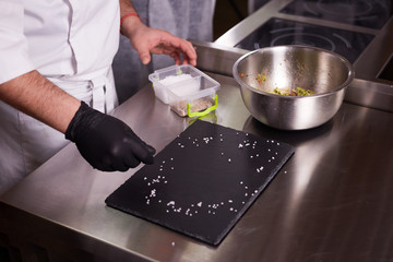 The process of cooking warm salad with veal. Hands of a chef in black gloves. Black slate board.
