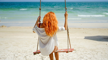 Beach summer vacation tropic palm style portrait of young beautiful girl on beach swing blue sea.Red haired woman swinging on the beach on Phu Quoc island, Vietnam. Happy  on tropical palm tree swing.
