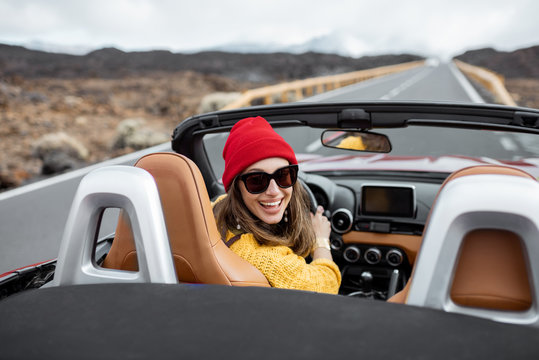 Portrait of a young woman traveling by convertible car on the picturesquare road on the volcanic valley. Carefree lifestyle and travel concept