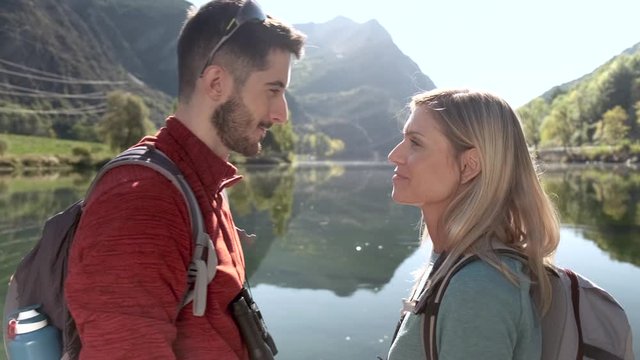 Video of two travel hikers in love kissing in front of the lake in mountain.