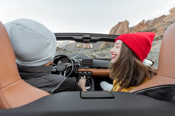 Couple driving a cabriolet on the mountain road, traveling by car and enjoying vacations, view from...