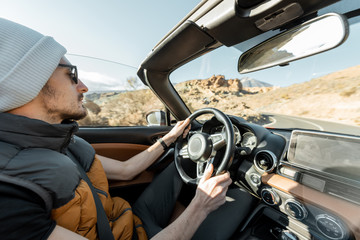 Man driving convertible car while traveling on the desert road. Carefree lifestyle and travel concept