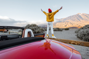 Woman dressed in bright sweater and hat enjoying great mountain landscapes while standing back on...