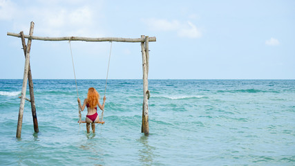 Beach summer vacation swing on th sea with young beautiful girl sitting on beach swing blue sea.Red...