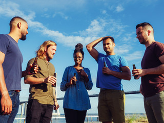Happy people talking and drinking beer during picnic. Good friends standing in circle with beer bottles. Concept of picnic