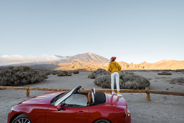 Woman enjoying great mountain landscapes while standing on the roadside with volcano on the background. Traveling by car on Tenerife island, wide view with copy space