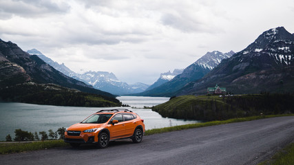 orange car parked on a hill overlooking mountains and a lake 