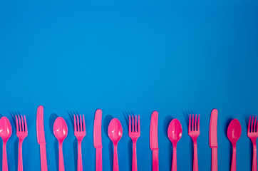 Flay lay photo of pink plastic disposable forks, spoons and knives lying on colorful background. Creative top view pattern.