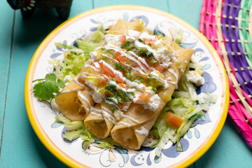 Mexican potato and cheese fried tacos also called flautas with green sauce on turquoise background