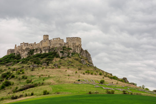 ruins of spis castle on a cloudy day in springtime. famous travel destination of slovakia. UNESCO heritage. grassy meadow at the foot of the hill.