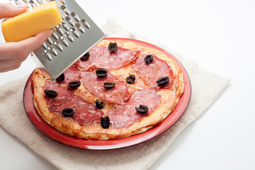 Hands grate cheese on pizza with salami, olives, on a white background. The concept of making pizza.