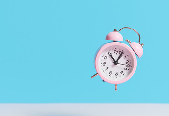 Pink alarm clock flies in the air on a blue background. Levitation effect