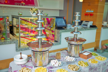 Chocolate fountain with fruits. Children birthday party . Homemade chocolate fountain fondue with marshmallow on a skewer dripping in chocolate sauce on blurred background and copy space .