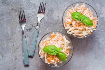American ready-to-eat cole slaw salad of cabbage, celery, carrots and apples with basil leaves in glass bowls in the ingredients for cooking on the table. Top view