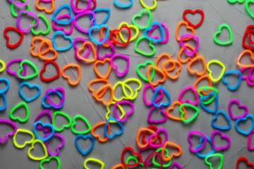 multi-colored elastic bands for weaving in the form of hearts are scattered on a concrete background