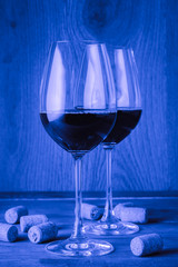 Two glasses with wine and cork on a wooden table. Blue tinted