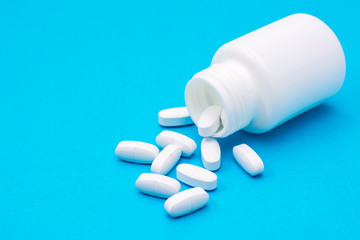 White large pills fall out of the bottle and scattered on a blue background. Medicines and packaging for them.