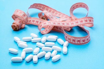 White oval pills in measuring tape on a blue background. The concept of losing weight with drugs.