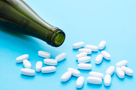 White Oval Pills An Empty Wine Bottle On A Blue Background. Drug Treatment Concept For Alcoholism. Fatal Addiction.