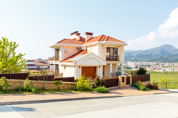 Fototapeta na wymiar Three-storey cottage in a classic Mediterranean style in white and peach color, Red tiled roof. Against the background of mountains in spring. Lifestyle. Realty