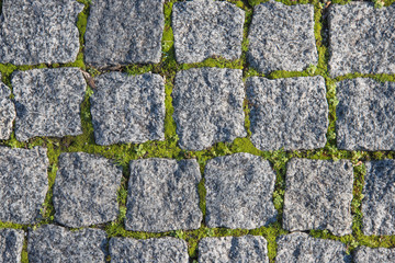 Paving stones made of natural stone. Paths for pedestrians. Beautiful square-shaped stones. Grass breaks through the rocks. The view from the top.