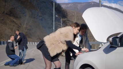 girls looks under the bumper of the car, men take it off on the phone