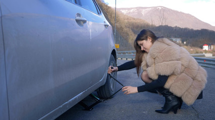 beautiful girl changing the wheel of a car parked on the roadside